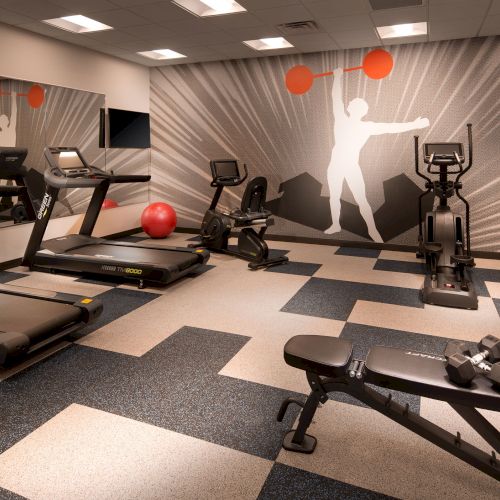 The image shows a gym with treadmills, stationary bikes, an incline bench with dumbbells, a red exercise ball, and a mural of a weightlifter on the wall.