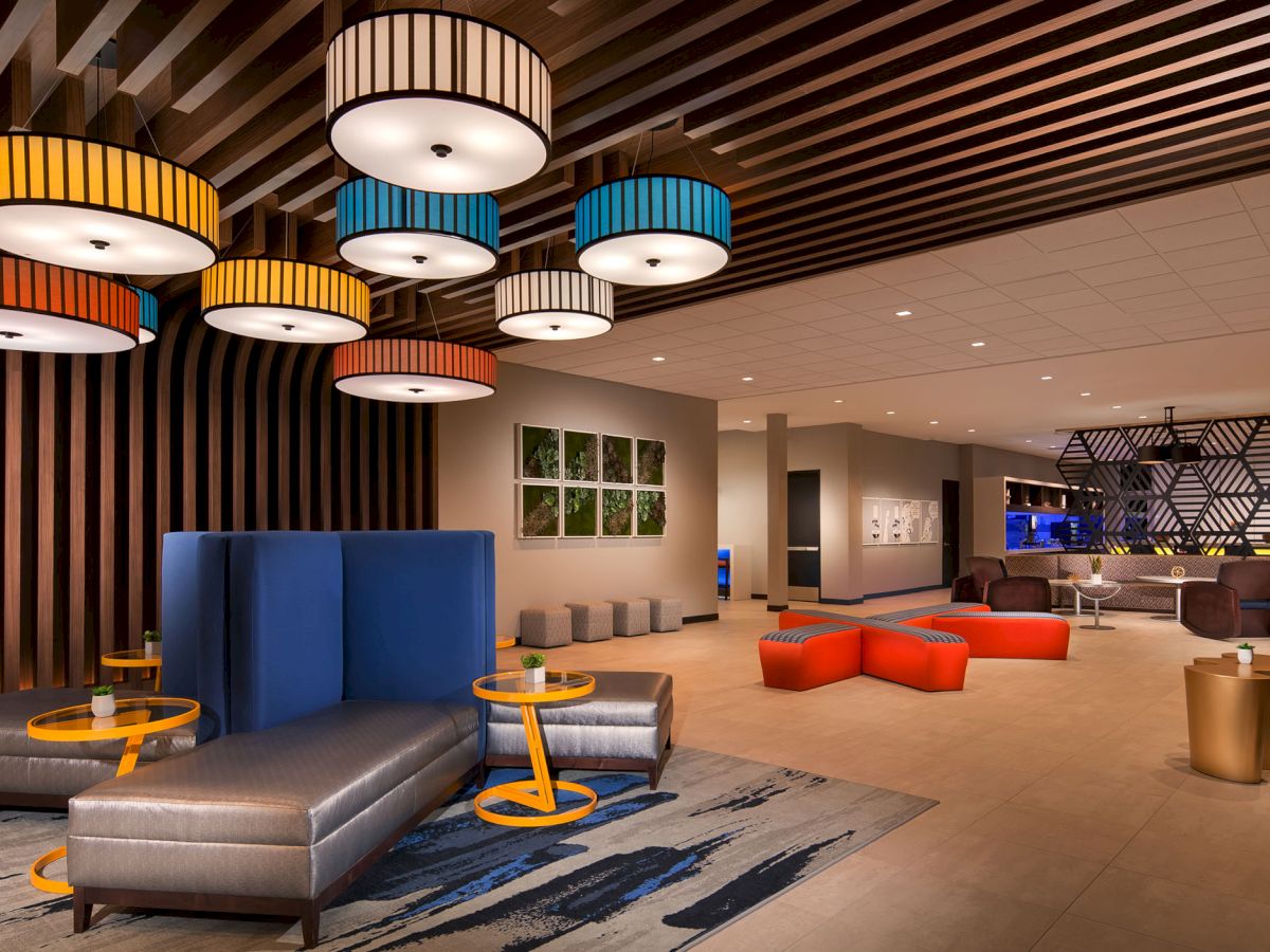 A modern lounge area with various seating arrangements, colorful hanging lights, and contemporary decor featuring geometric patterns and wood accents.