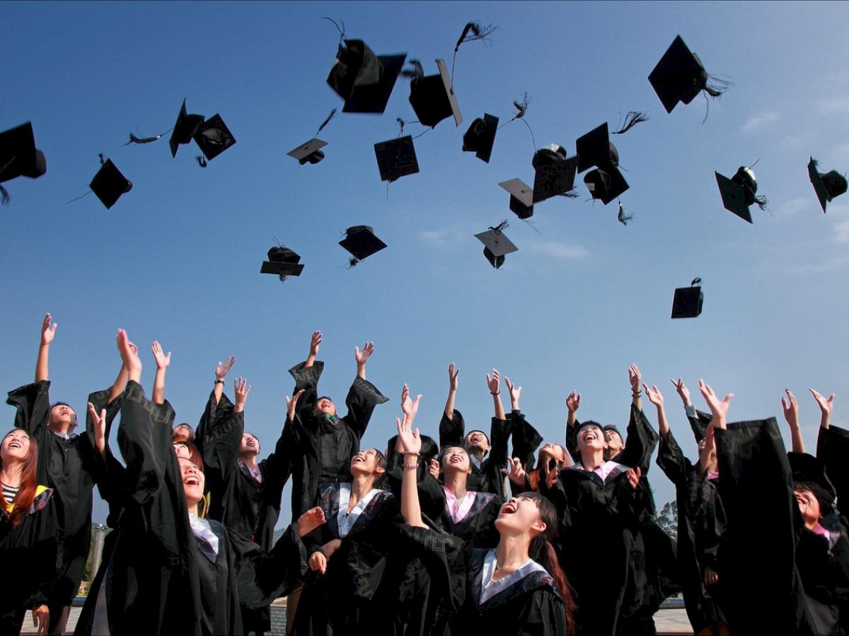 Students in graduation robes celebrating by tossing their caps into the air against a clear blue sky.