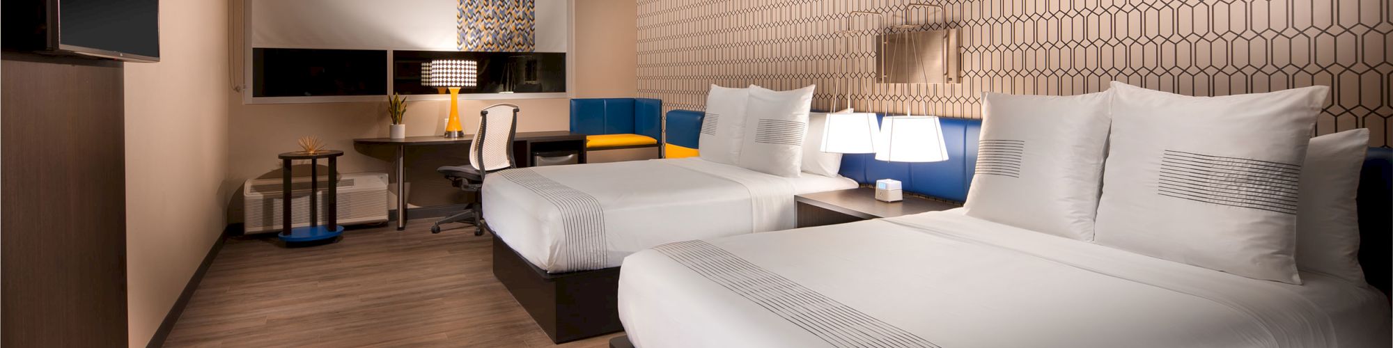 This image shows a modern hotel room with two neatly made double beds, a large TV, a desk with a chair, and contemporary decor on the wall.