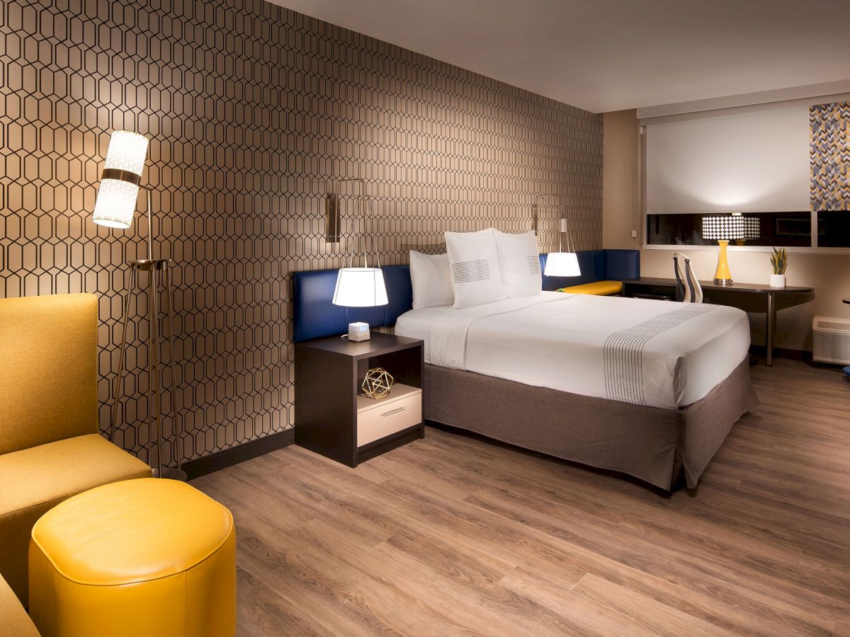 A modern hotel room with a large bed, stylish furniture, a seating area, and contemporary lighting and decor.