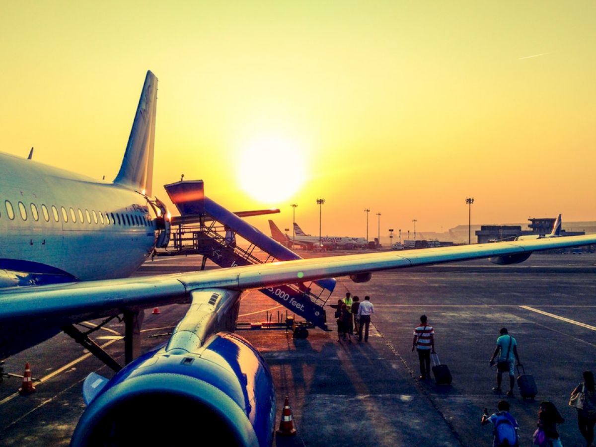 An airplane on a runway at sunset with passengers walking towards it and the ambiance glowing in a warm, golden light.