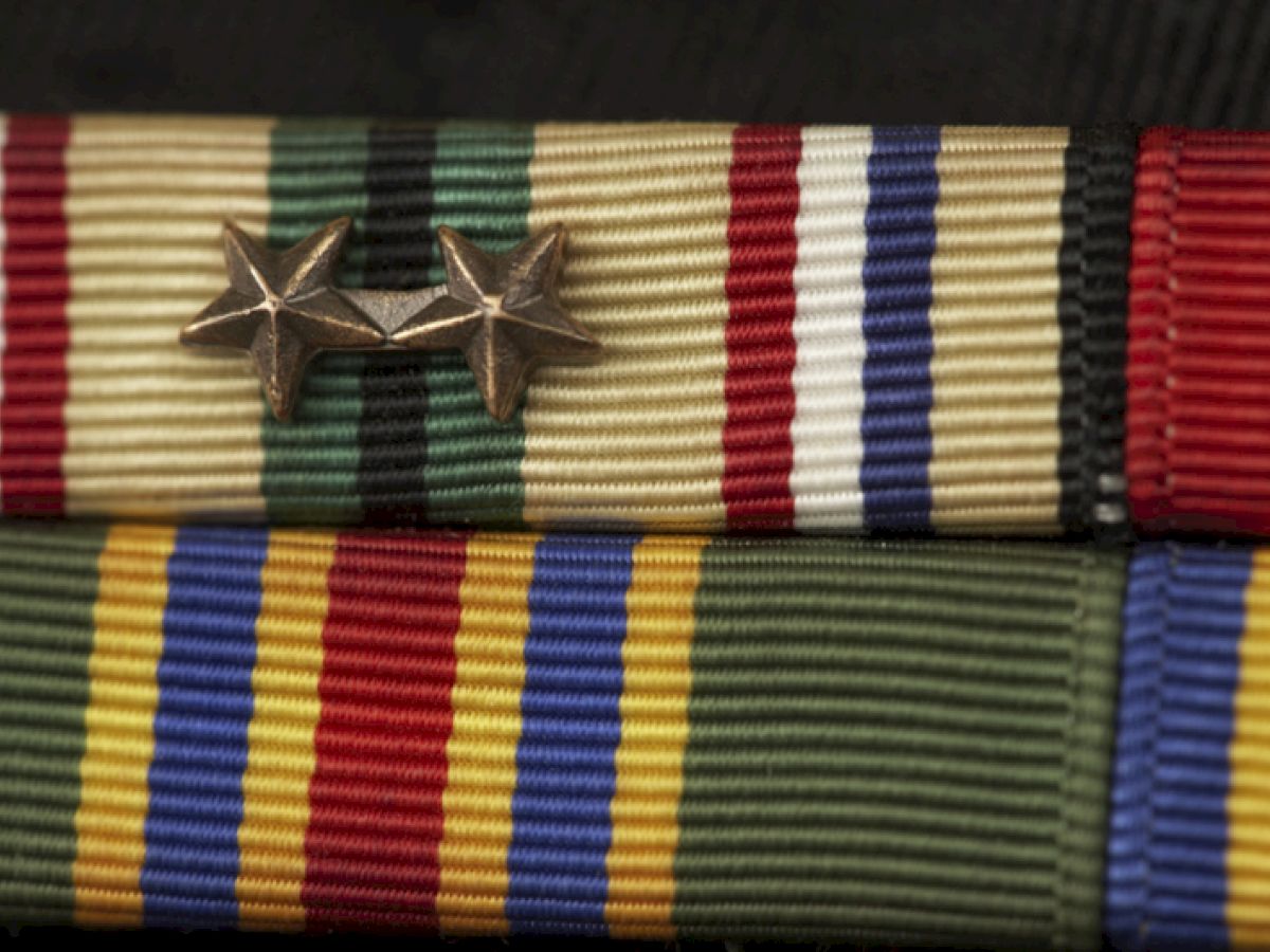 The image shows military ribbons and medals adorned with two bronze stars as decorations, representing commendations and achievements.