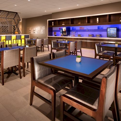 The image shows a modern dining area with tables, chairs, and a bar. The lighting is warm, and the decor is contemporary and clean.