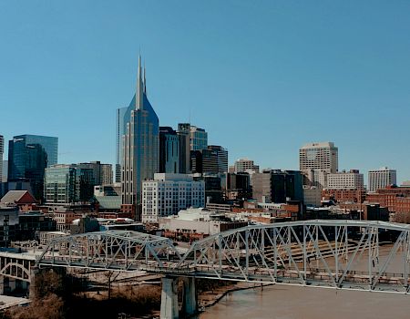 Downtown skyline with skyscrapers and a white steel bridge over a river under a clear blue sky.