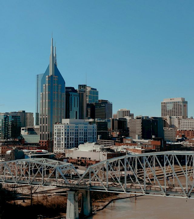 Downtown skyline with skyscrapers and a white steel bridge over a river under a clear blue sky.