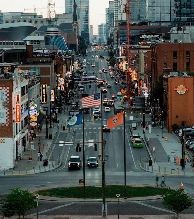 A busy downtown street in Chicago at dusk, lined with brick buildings, cars and pedestrians, plus the Hard Rock Café sign and flags.