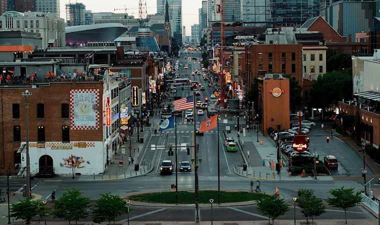 A busy downtown street in Chicago at dusk, lined with brick buildings, cars and pedestrians, plus the Hard Rock Café sign and flags.